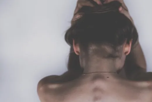 Persona a torso nudo con le mani sulla testa, vista da dietro.