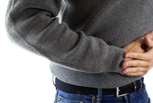 Persona con maglione grigio che si tiene la pancia per il dolore.