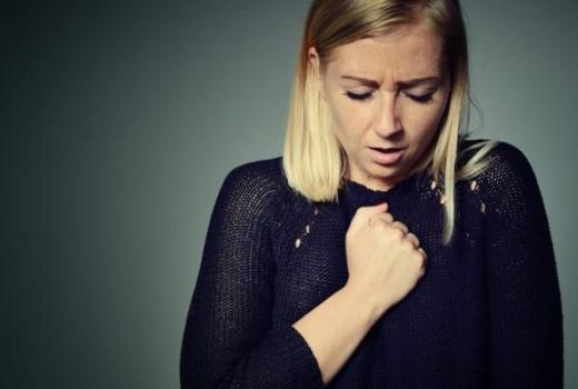 Donna con mano sul petto, sembra provare dolore o disagio.