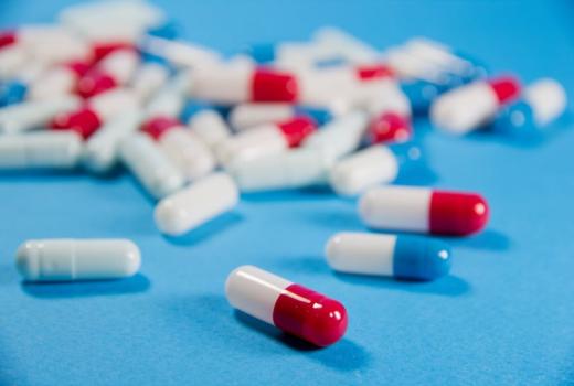 Capsule farmaceutiche rosse, bianche e blu su sfondo blu.